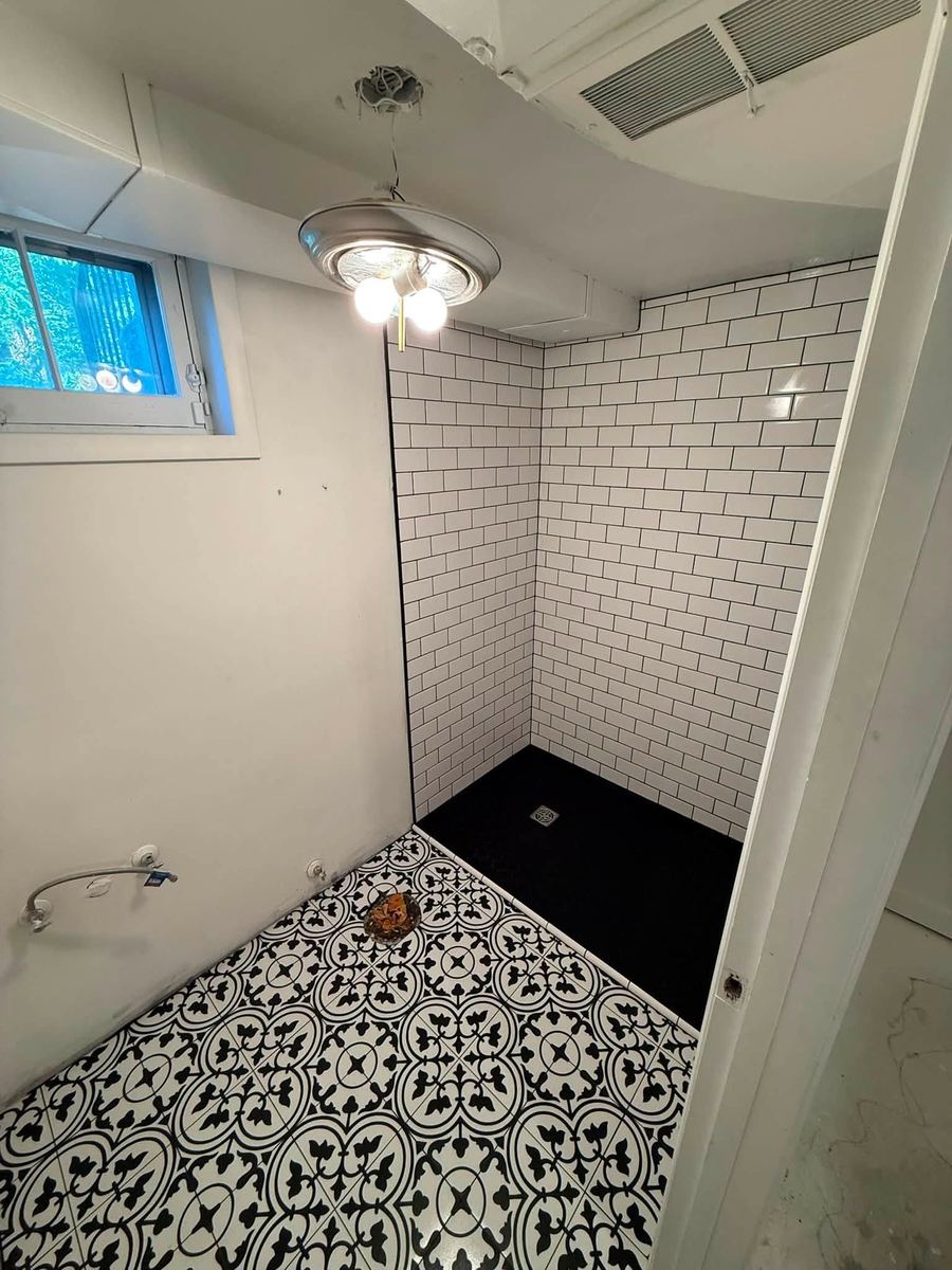 Walk-in shower in white subway tile with black grout next to a patterned black and white floor tile