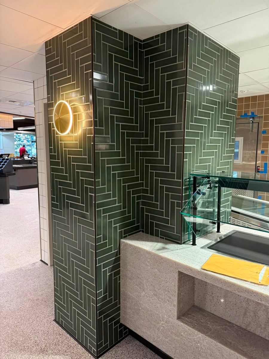Deep green glazed tile laid in a basketweave pattern wrapping a column and wall in a commercial servery