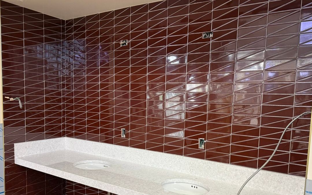 Commercial restroom wall tiled in deep red glazed tile laid in a diagonal pattern behind a two-basin stone vanity