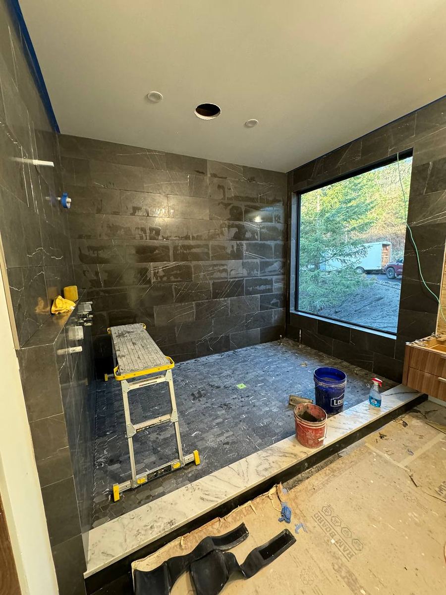 Walk-in shower lined in dark slate-look tile with a picture window above the bench