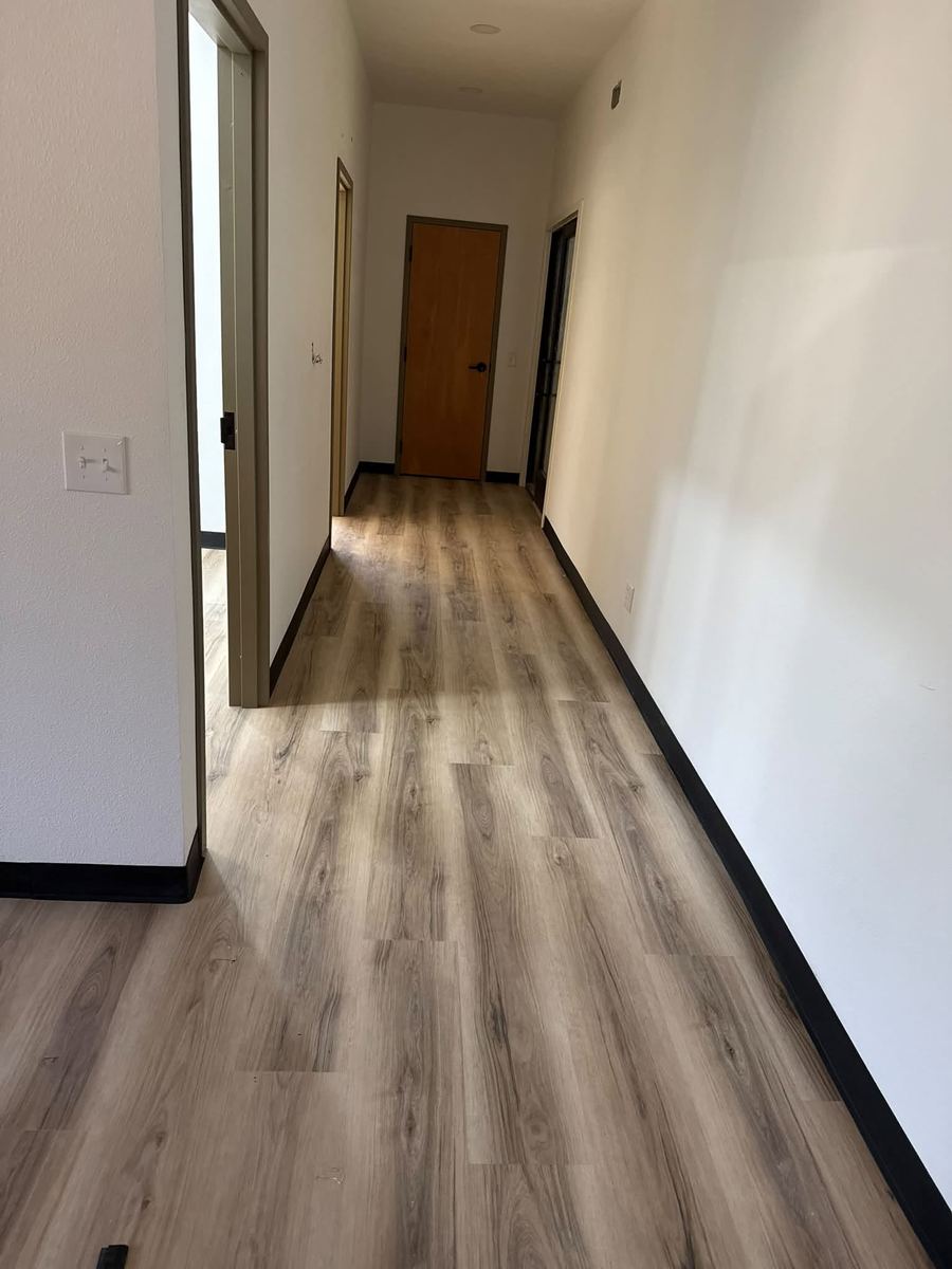 Wood-look luxury vinyl plank flooring installed down a hallway with black vinyl base trim