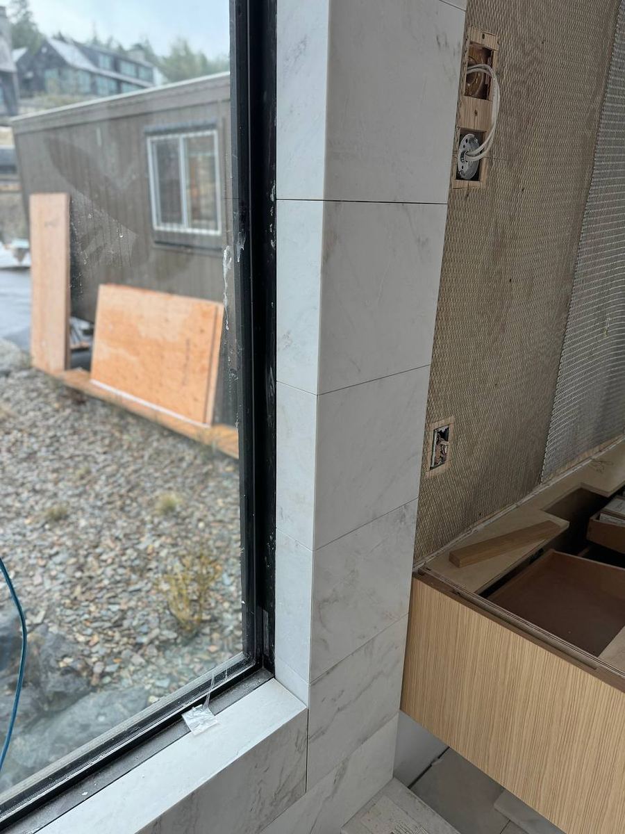 Marble-look tile wrapped around a bathroom window return beside a floating oak vanity