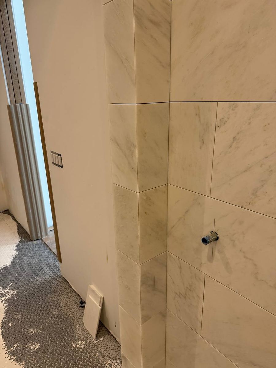 Outside corner of a marble-look tiled wall finished with a tight mitred joint and a shower valve outlet