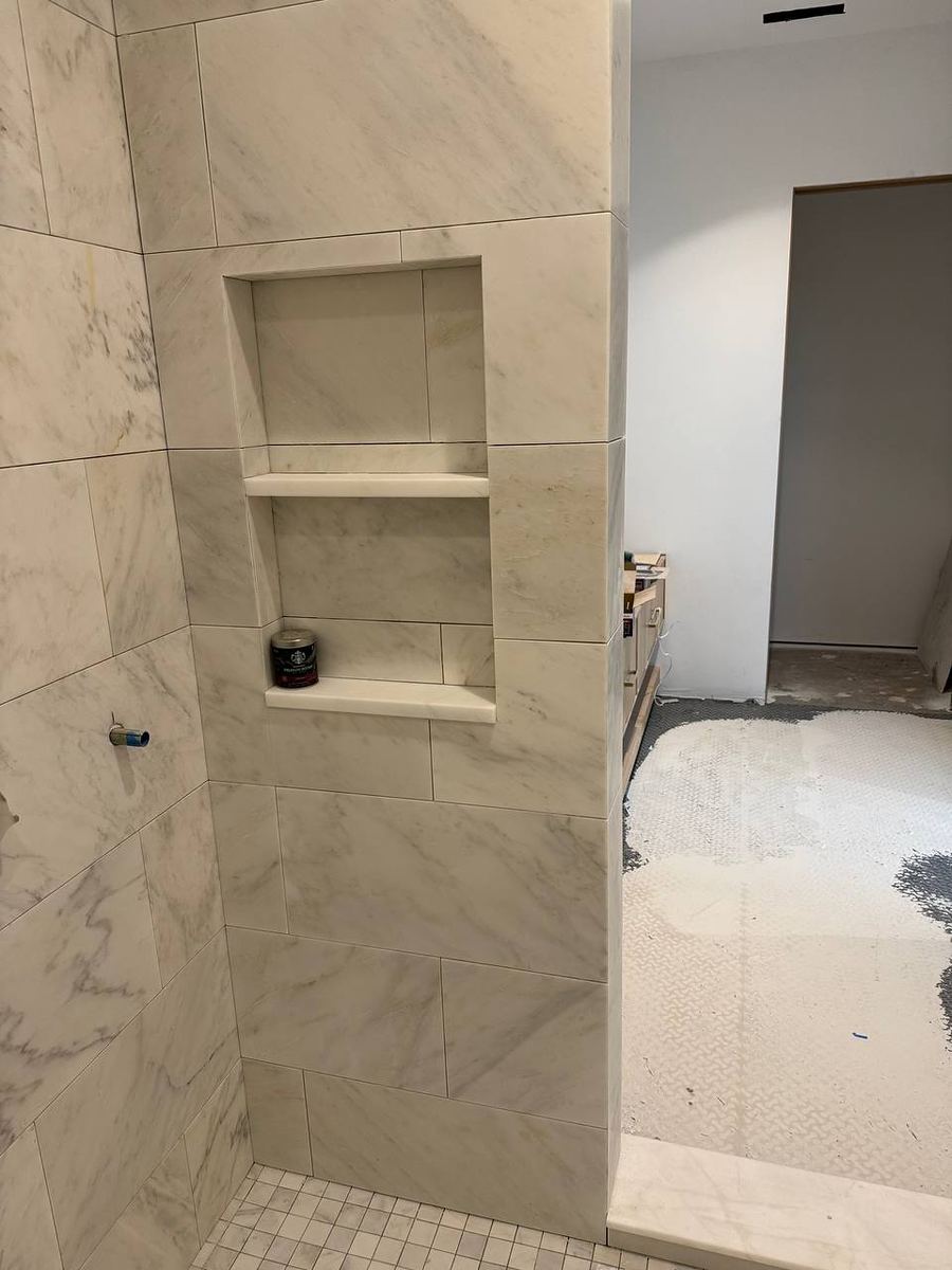 Two-shelf recessed shower niche framed in white marble-look tile with mitred edges