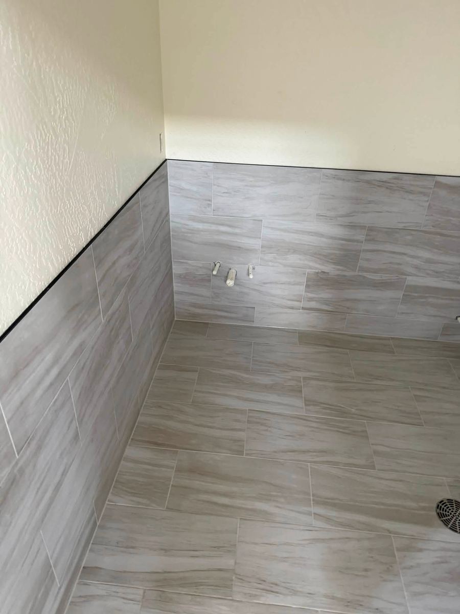 Grey stone-look floor tile continuing up the wall as a tiled wainscot with a black edge trim