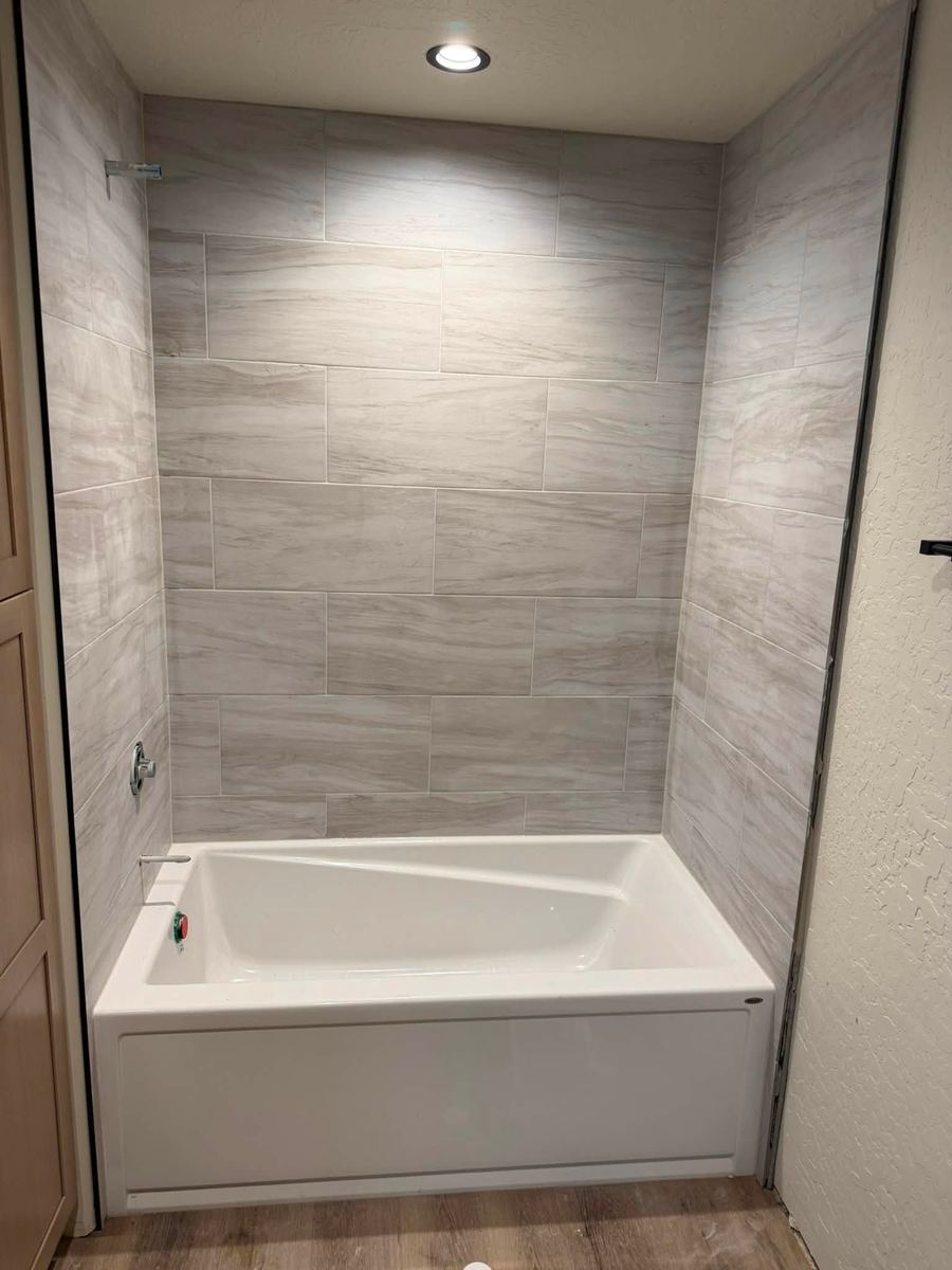 Alcove tub with a light stone-look tile surround running full height to the ceiling