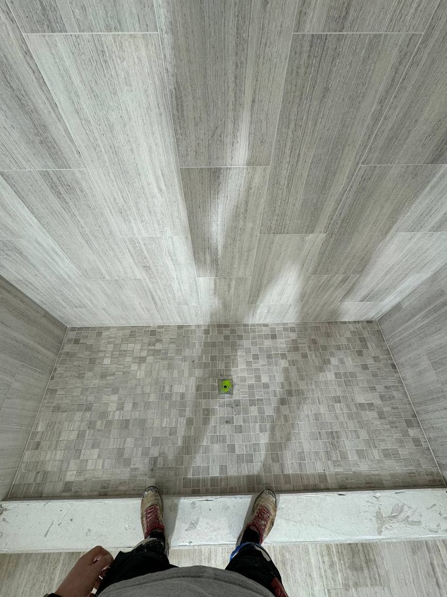 Grey wood-look plank floor meeting a mosaic-tiled shower pan across a stone threshold