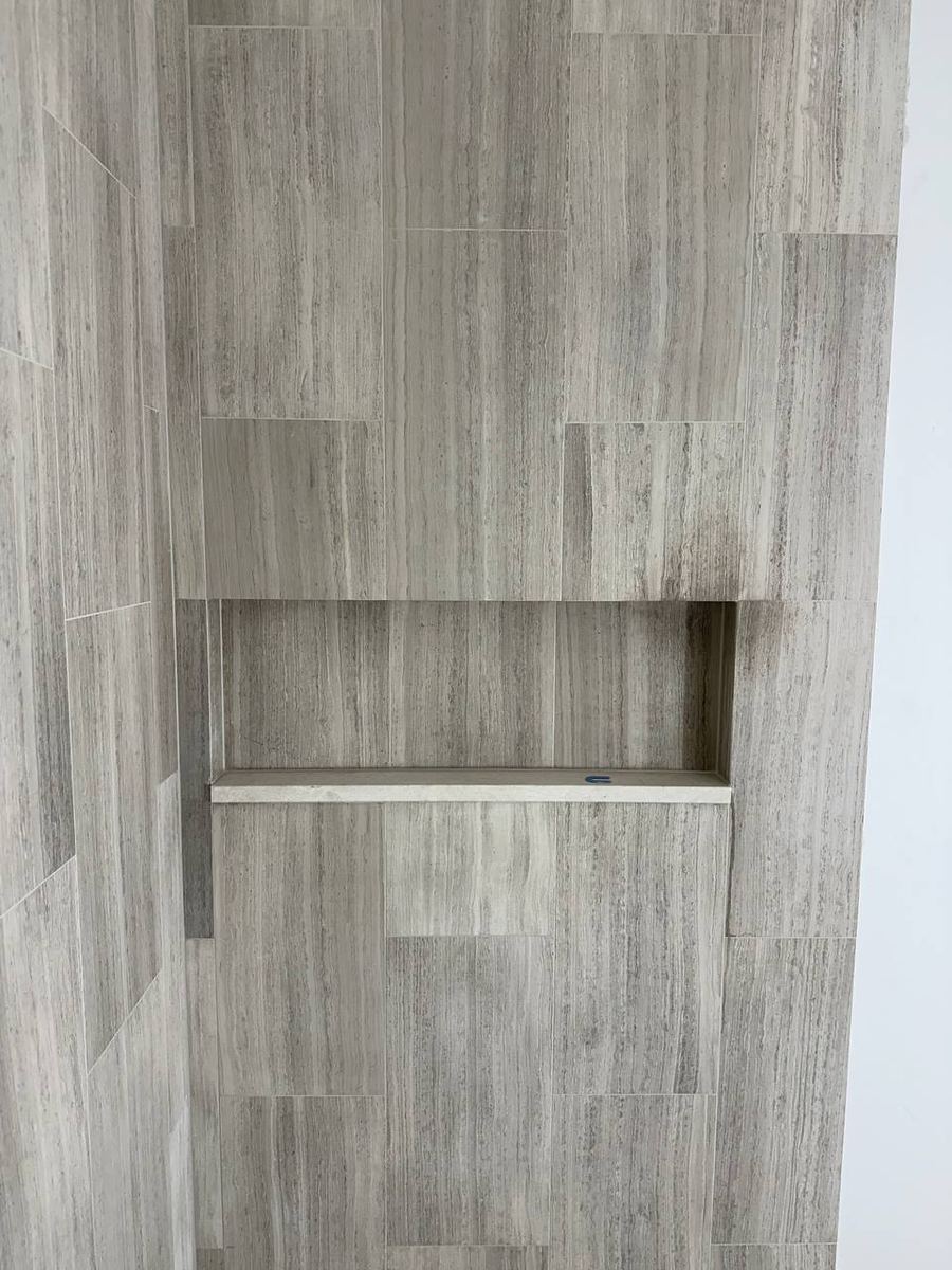 Full-width shower niche set into grey wood-look tile with a solid stone shelf